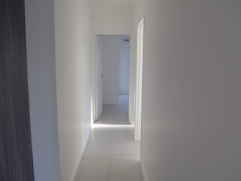 A clean, minimalist hallway featuring neutral tiled flooring and white interior doors, providing a bright and seamless transition between rooms.