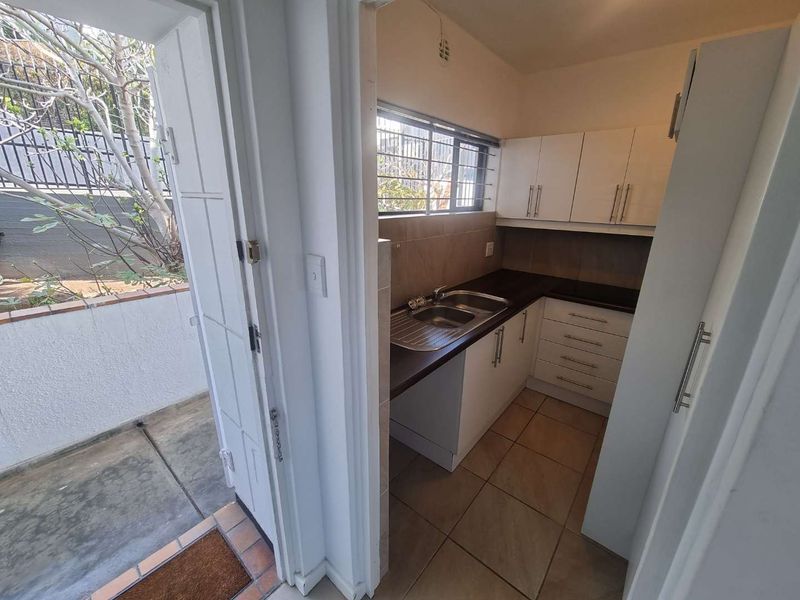 A compact, functional scullery area featuring built-in cabinetry, a stainless steel sink, and tiled flooring, with direct access to an outdoor patio space.