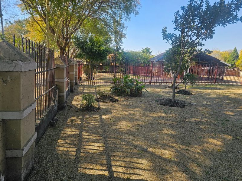 A spacious garden area featuring established trees, landscaped beds, and secure metal perimeter fencing with masonry pillars.