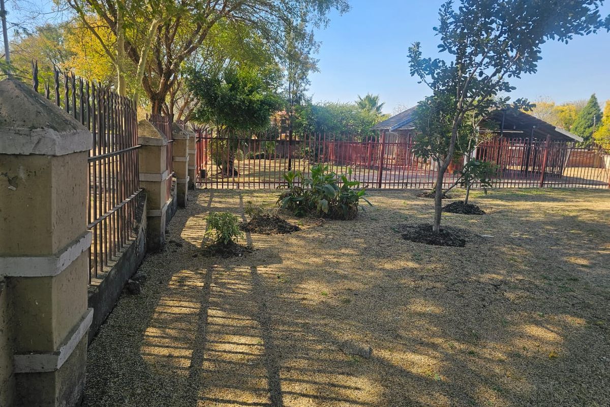 A spacious garden area featuring established trees, landscaped beds, and secure metal perimeter fencing with masonry pillars.