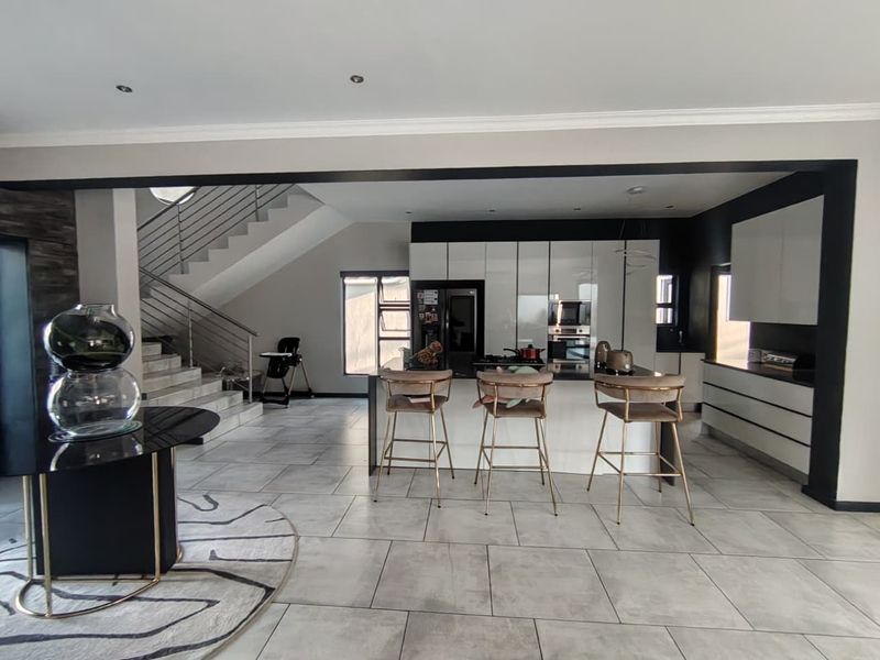 Modern open-plan kitchen featuring a central island, sleek cabinetry, built-in appliances, and tiled flooring, seamlessly connected to a staircase area.