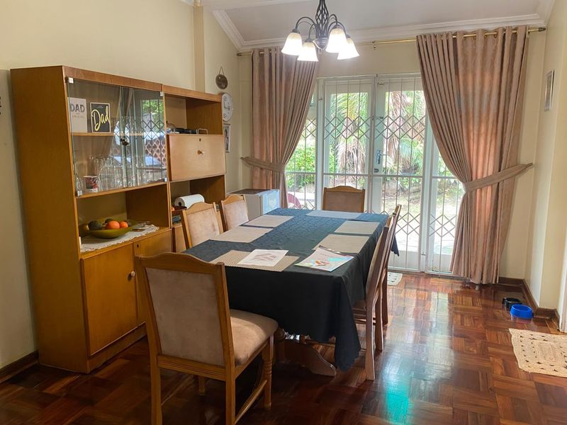 A dining room featuring warm parquet flooring, a coved ceiling, and glass sliding doors with security gates providing access to the garden.