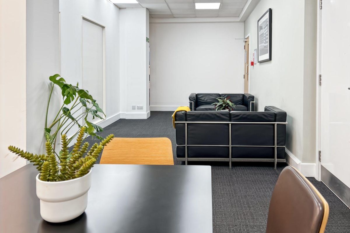 A professional office space featuring a suspended ceiling, recessed lighting, and dark carpet flooring, providing a clean and functional work environment.