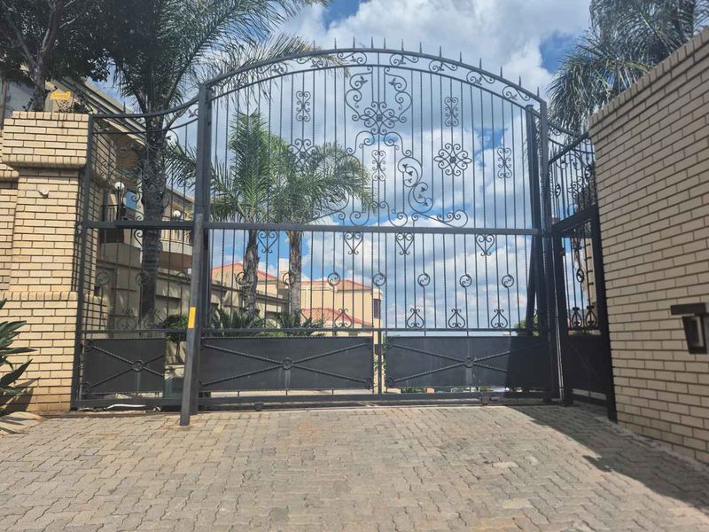 A secure entrance featuring a decorative wrought iron gate set within a brick boundary wall and paved driveway.