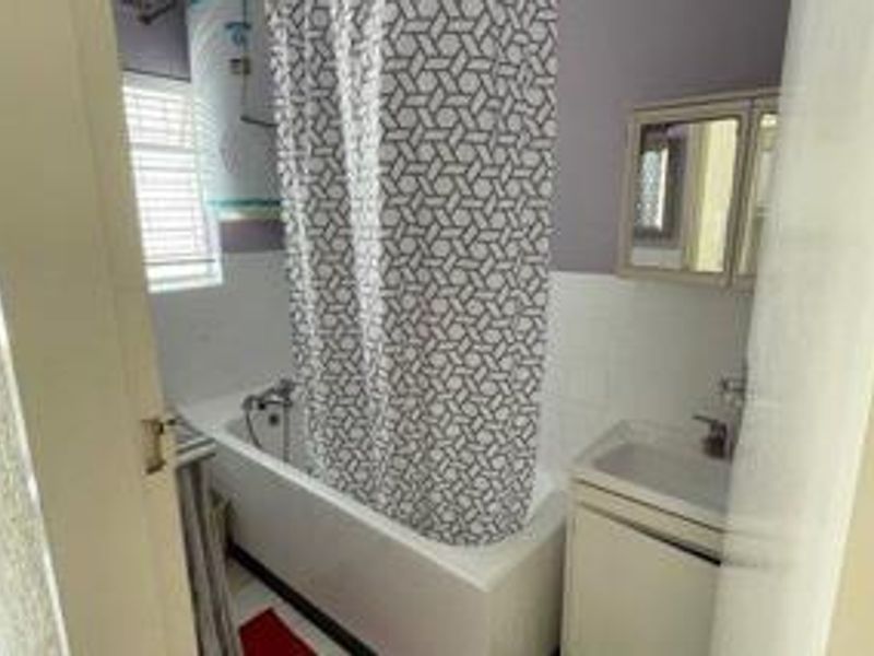A compact bathroom featuring a bathtub with shower mixer, a vanity basin, and a wall-mounted medicine cabinet, requiring some cosmetic updates.