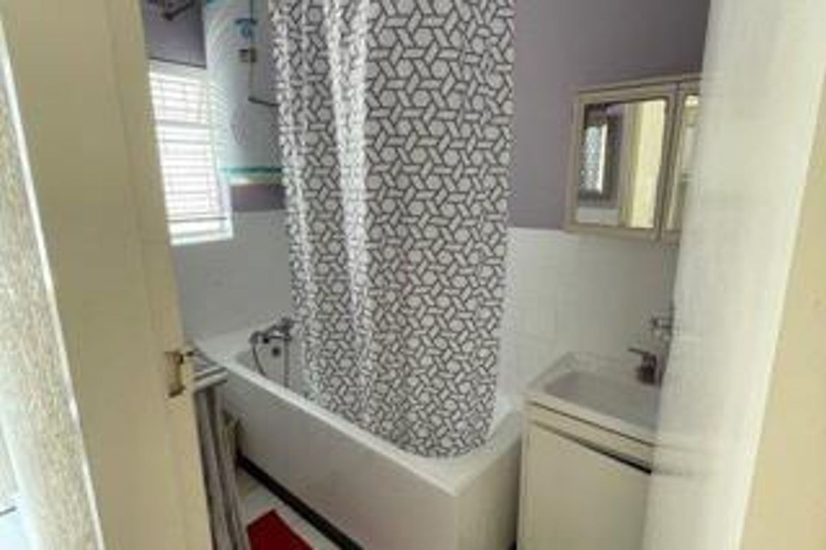 A compact bathroom featuring a bathtub with shower mixer, a vanity basin, and a wall-mounted medicine cabinet, requiring some cosmetic updates.