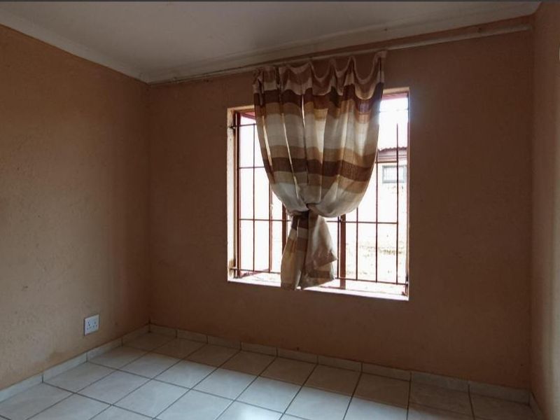 A vacant bedroom featuring tiled flooring, security bars on the window, and neutral wall finishes, offering a blank canvas for potential updates.