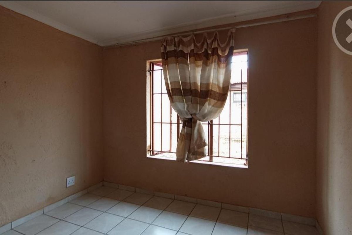 A vacant bedroom featuring tiled flooring, security bars on the window, and neutral wall finishes, offering a blank canvas for potential updates.