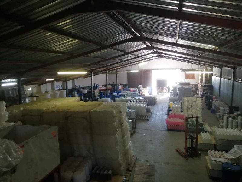 Spacious industrial warehouse featuring high-clearance corrugated metal roofing, exposed steel trusses, concrete flooring, and a large roller door for loading access.