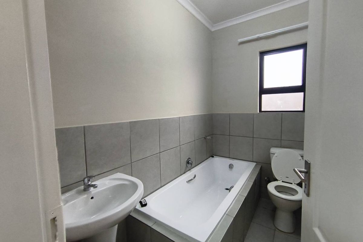 A functional bathroom featuring a pedestal basin, a built-in bathtub with tiled surround, and a standard toilet.