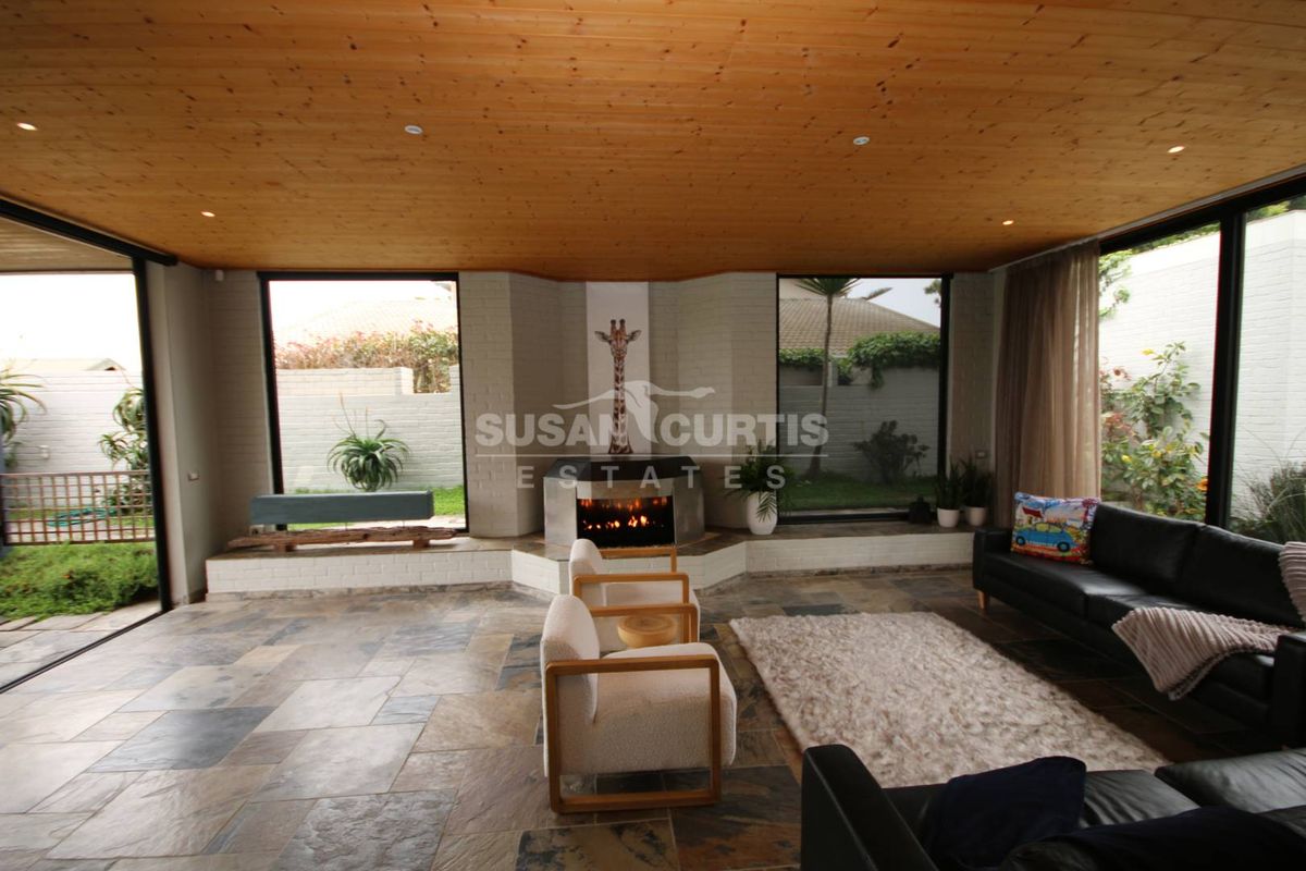 Spacious living room featuring a built-in fireplace, natural stone flooring, and a warm timber ceiling with expansive windows overlooking the garden.