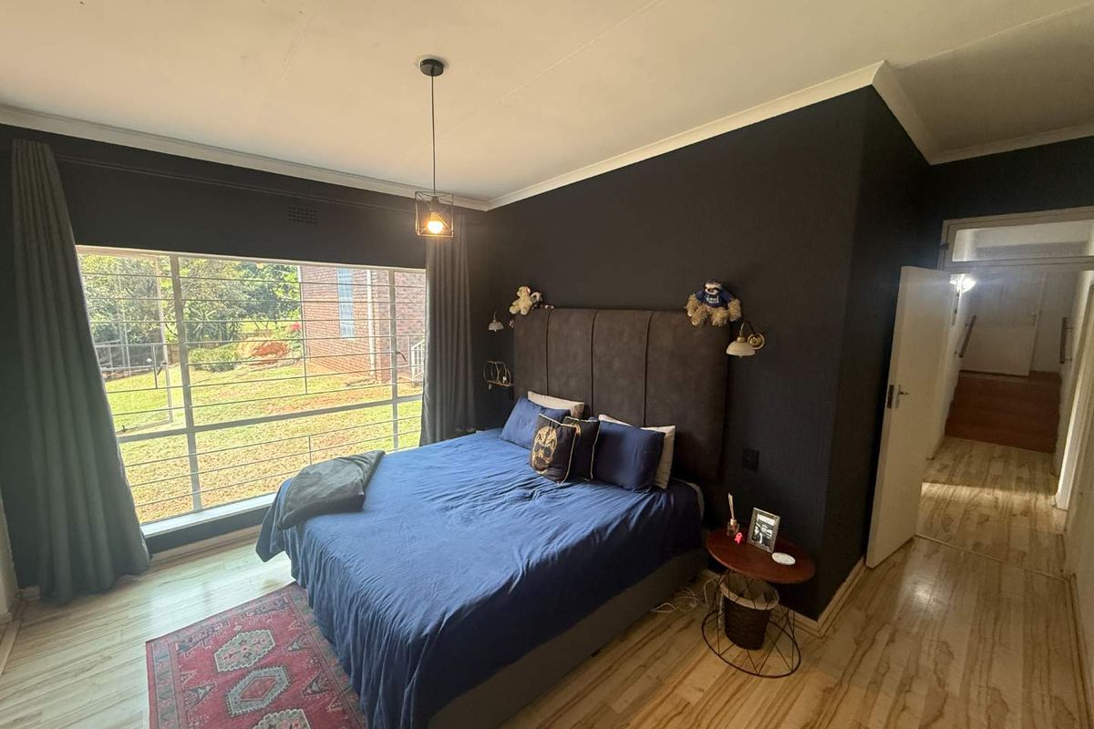 A well-lit bedroom featuring laminate flooring, a large window with security bars, and a dark accent wall.