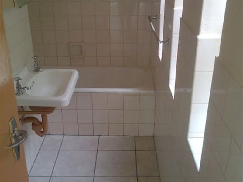 A dated bathroom featuring a bathtub, wall-mounted basin, and tiled finishes, requiring modernization to improve functionality and aesthetic appeal.