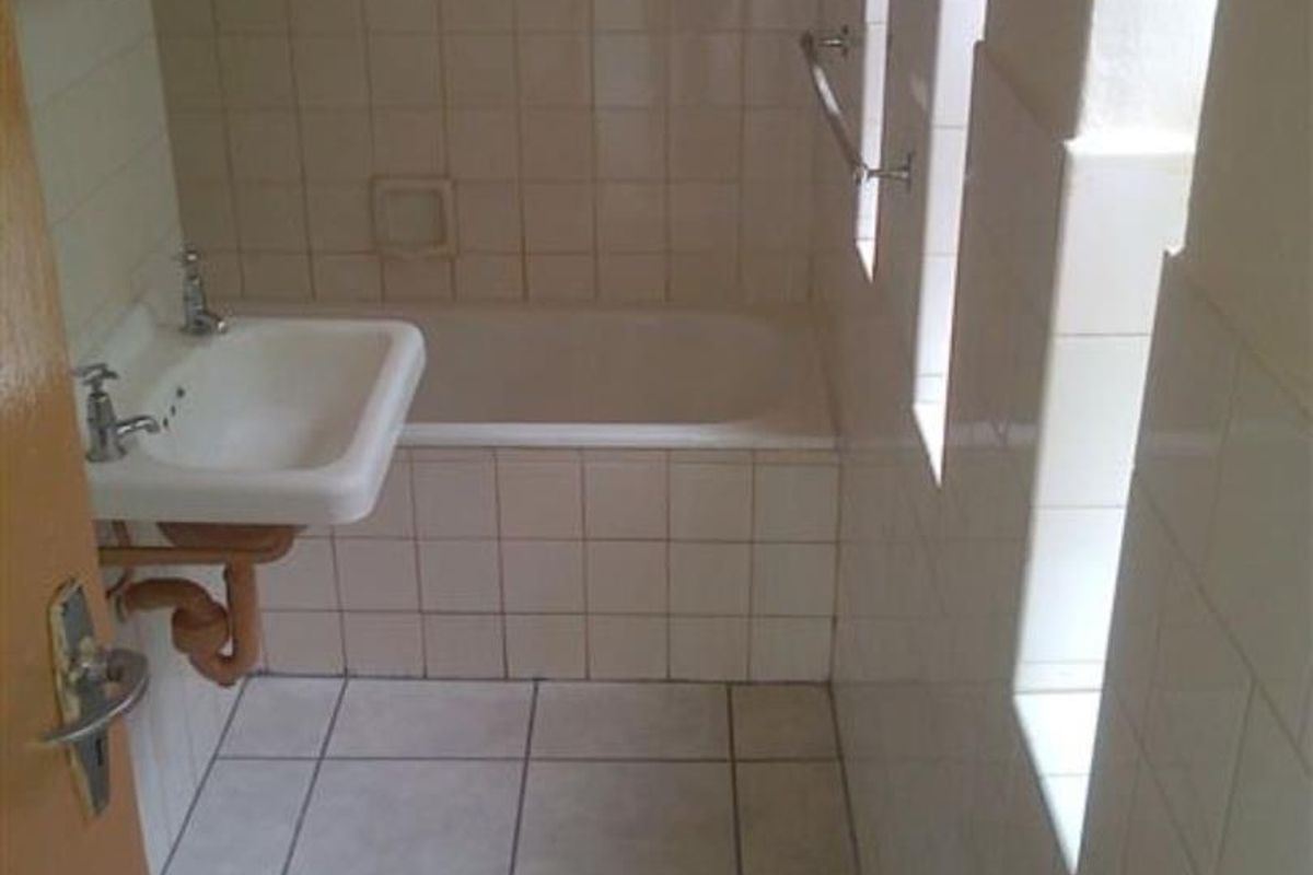 A dated bathroom featuring a bathtub, wall-mounted basin, and tiled finishes, requiring modernization to improve functionality and aesthetic appeal.