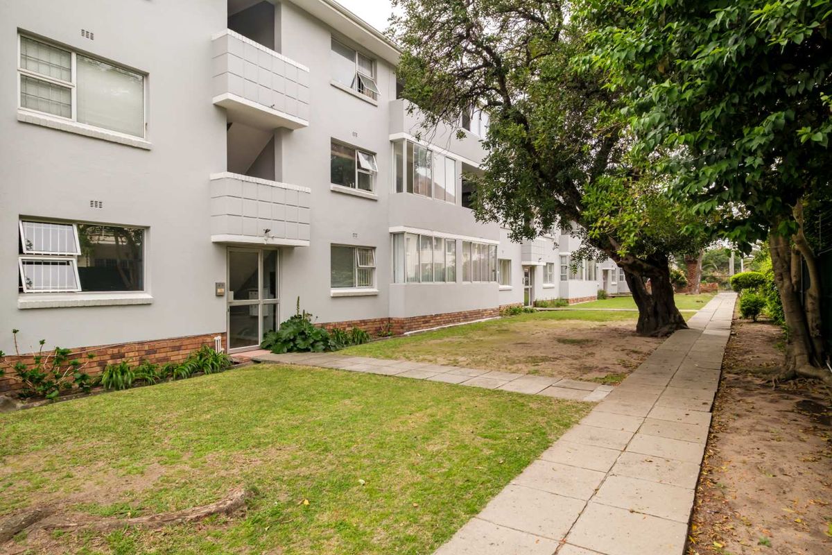 Rear view of the apartment building featuring a paved walkway, established lawn, and mature trees along the exterior facade.