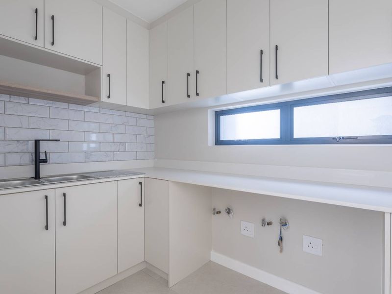 Modern, well-appointed laundry room featuring sleek cabinetry, marble-look subway tile backsplash, stainless steel sink, and dedicated plumbing connections for appliances.