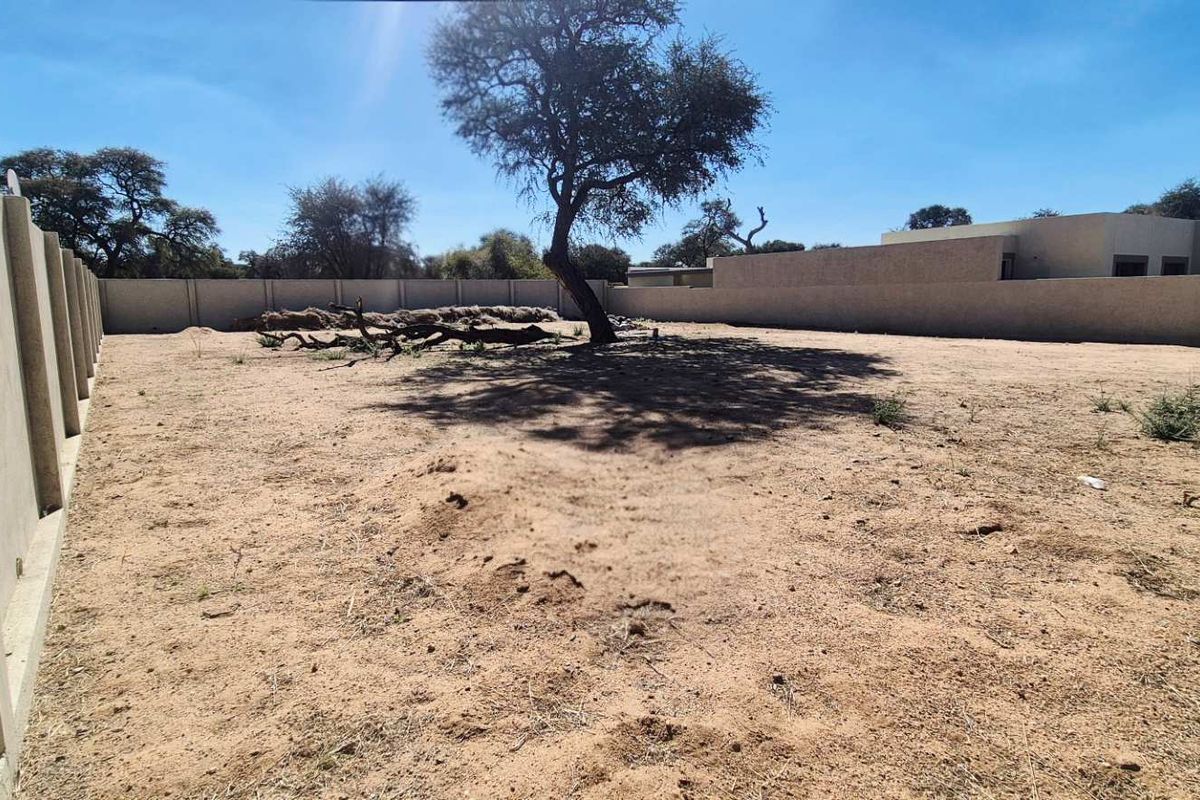 A vacant residential plot featuring a level sandy surface enclosed by a perimeter boundary wall.