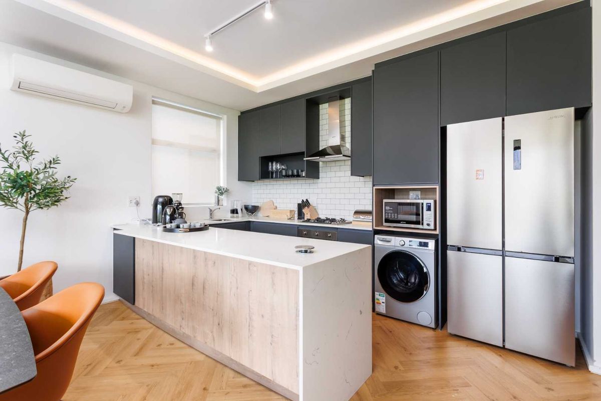 Modern kitchen featuring dark cabinetry, stone countertops, a breakfast island, subway tile backsplash, integrated appliances, and herringbone wood flooring.