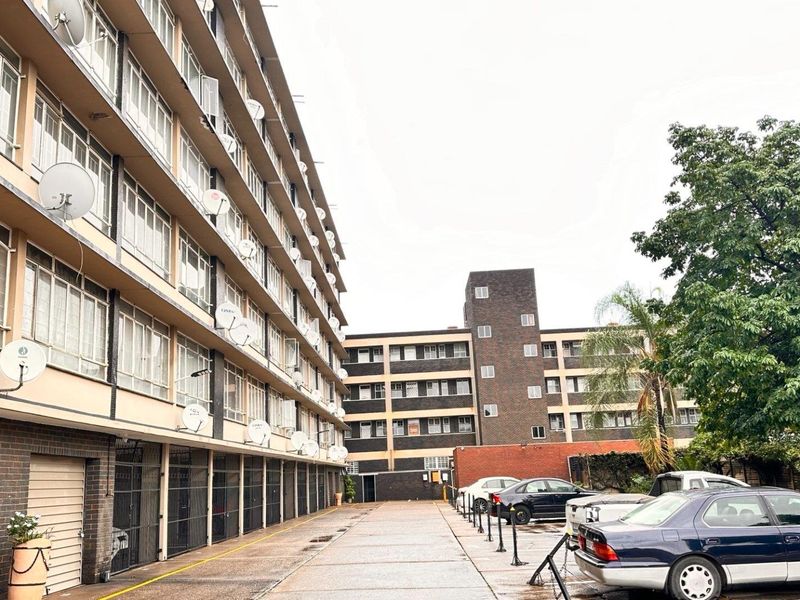Exterior view of a multi-story apartment complex featuring a paved driveway, ground-level garage access, and multiple satellite dish installations.