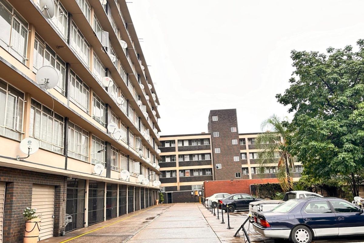 Exterior view of a multi-story apartment complex featuring a paved driveway, ground-level garage access, and multiple satellite dish installations.