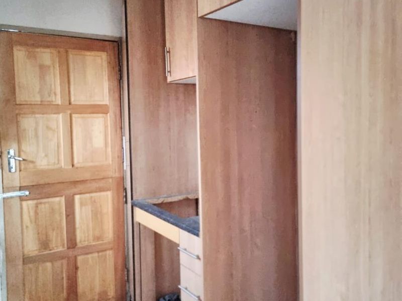 A compact scullery or utility area featuring built-in wooden cabinetry, laminate countertops, and tiled flooring, currently awaiting a sink installation.