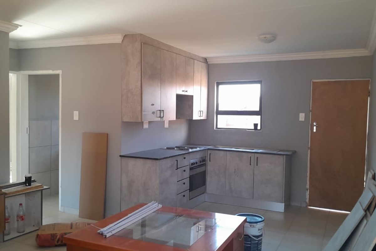 A functional kitchen space featuring modern grey cabinetry, built-in oven and hob, and tiled flooring, currently in a state of completion.