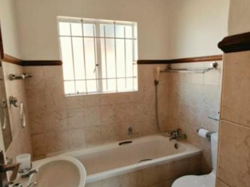 A functional bathroom featuring a pedestal basin, bathtub, and toilet with neutral wall and floor tiling.