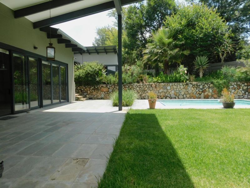 A spacious covered patio area featuring stone retaining walls, a swimming pool, and large sliding glass doors leading into the home.