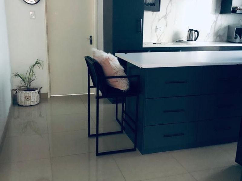 Modern kitchen featuring a dark-toned island, stone countertops, marble-look splashback, and open shelving, complemented by sleek tiled flooring.