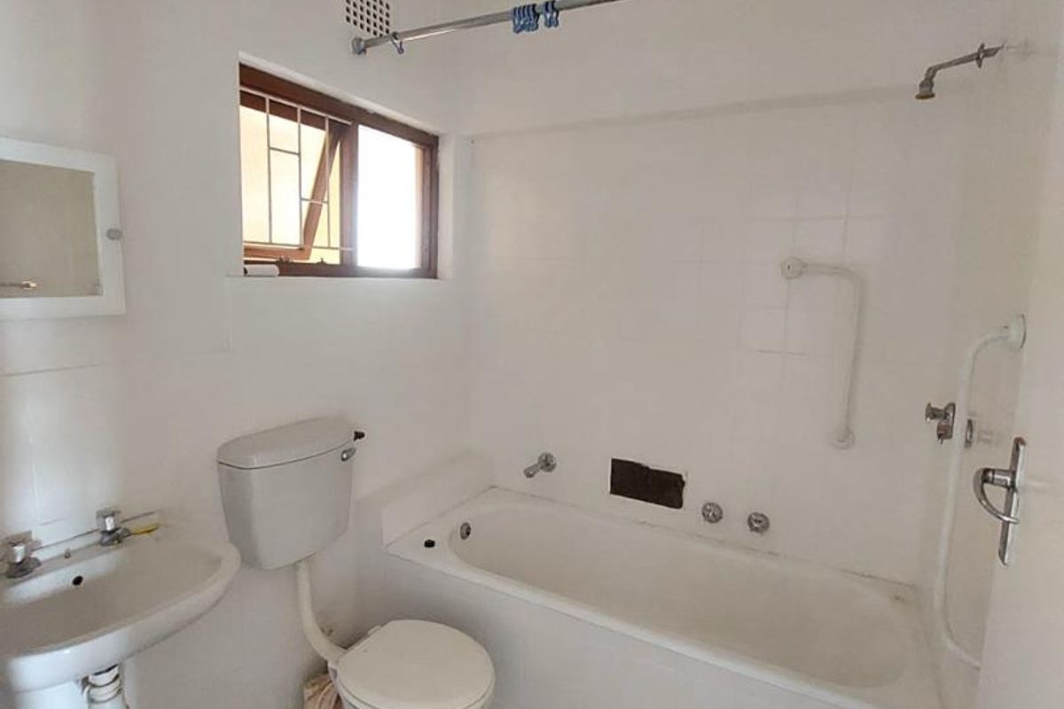 A functional bathroom featuring a bathtub, pedestal basin, and toilet, with tiled flooring and basic wall-mounted fixtures, ready for modernization.
