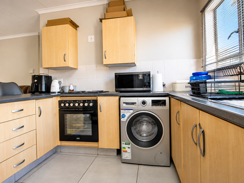 Functional kitchen featuring light wood cabinetry, built-in oven and hob, integrated washing machine, and tiled splashback with ample counter space.