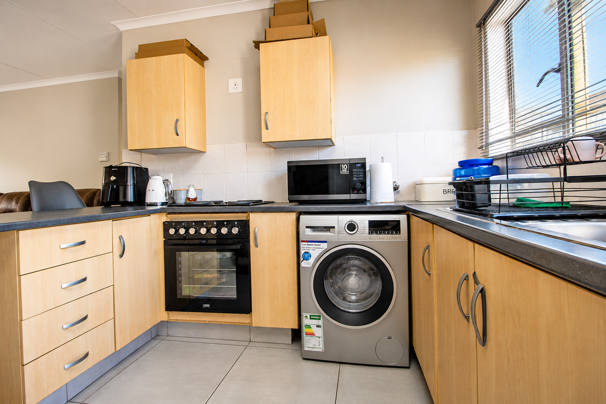 Functional kitchen featuring light wood cabinetry, built-in oven and hob, integrated washing machine, and tiled splashback with ample counter space.