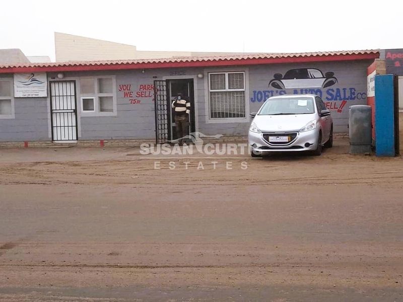 Front elevation of an industrial property featuring a single-story structure with security gates and signage, situated on an unpaved lot.