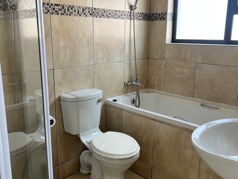 A functional bathroom featuring a bathtub with handheld shower, separate shower enclosure, pedestal basin, and neutral floor-to-ceiling wall tiling.