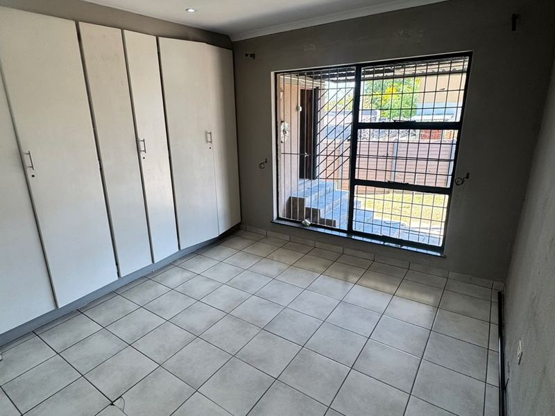 An empty bedroom featuring tiled flooring, built-in cupboards, and a window fitted with security bars.