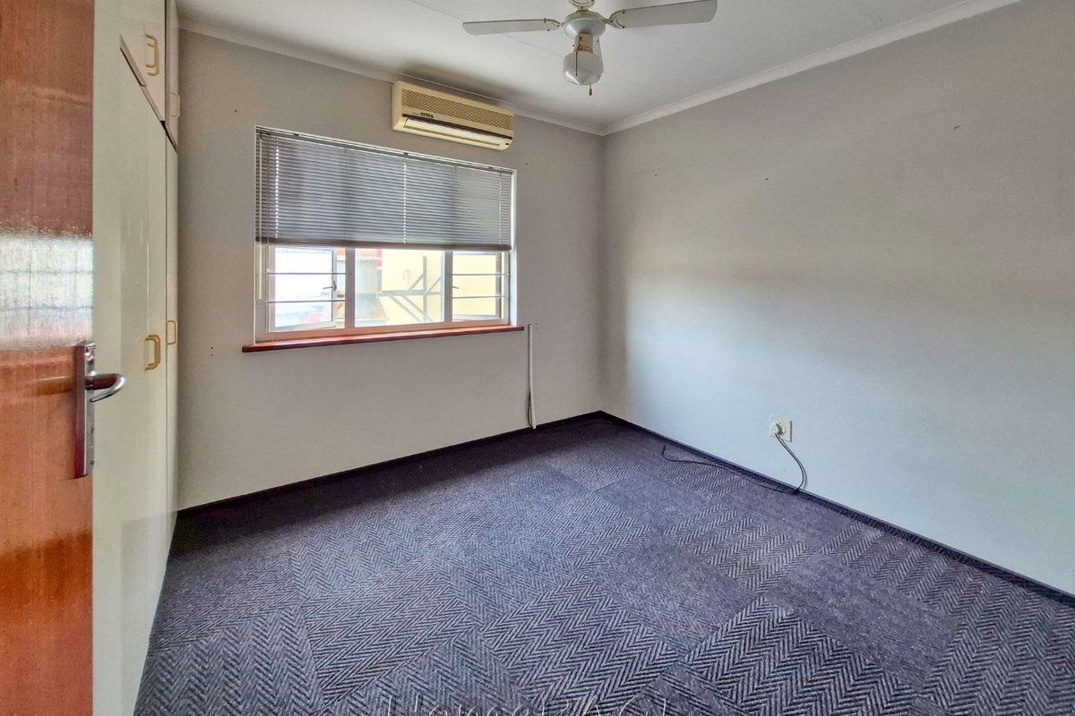 A functional bedroom featuring built-in cabinetry, a ceiling fan, and a wall-mounted air conditioning unit, finished with carpeted flooring.