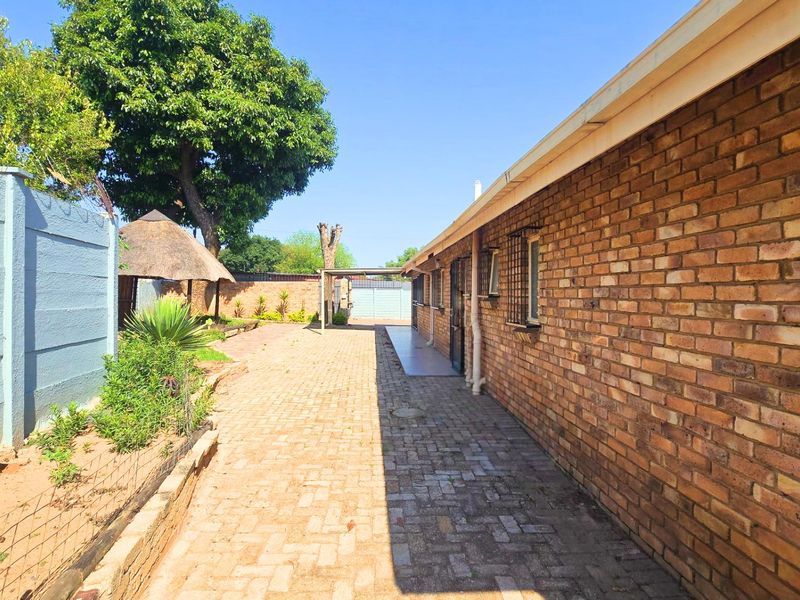 Rear exterior view featuring brick paving, a face brick wall, and a small thatch roof gazebo in the garden area.
