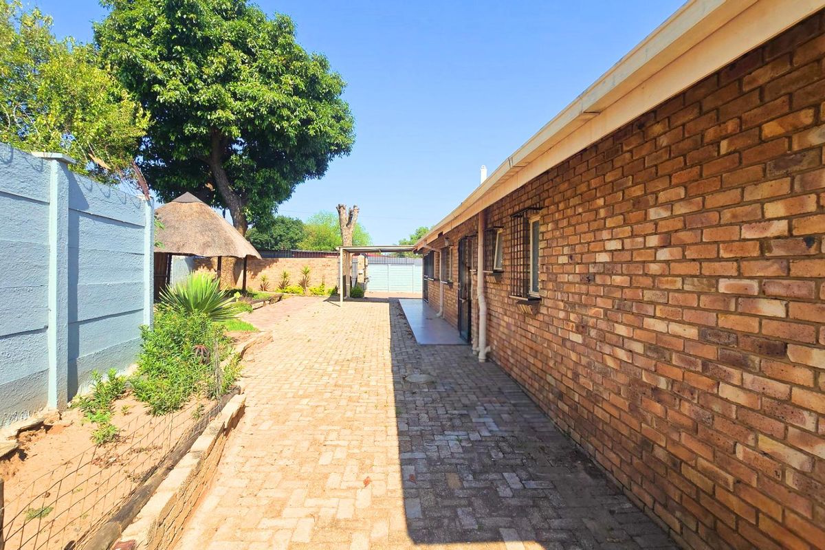 Rear exterior view featuring brick paving, a face brick wall, and a small thatch roof gazebo in the garden area.