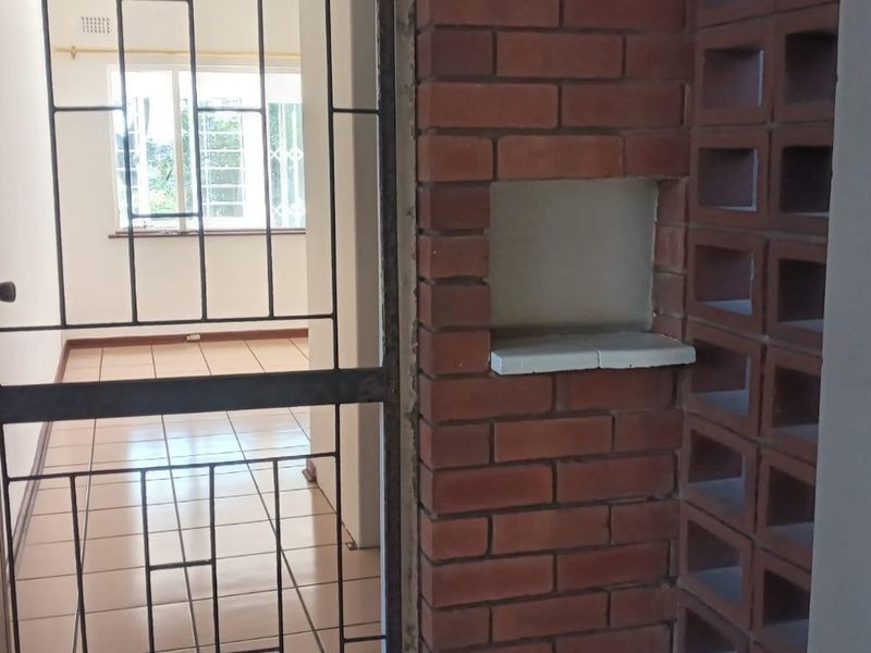 Entrance area featuring a security gate, brick feature wall, and breeze block detailing with tiled flooring.