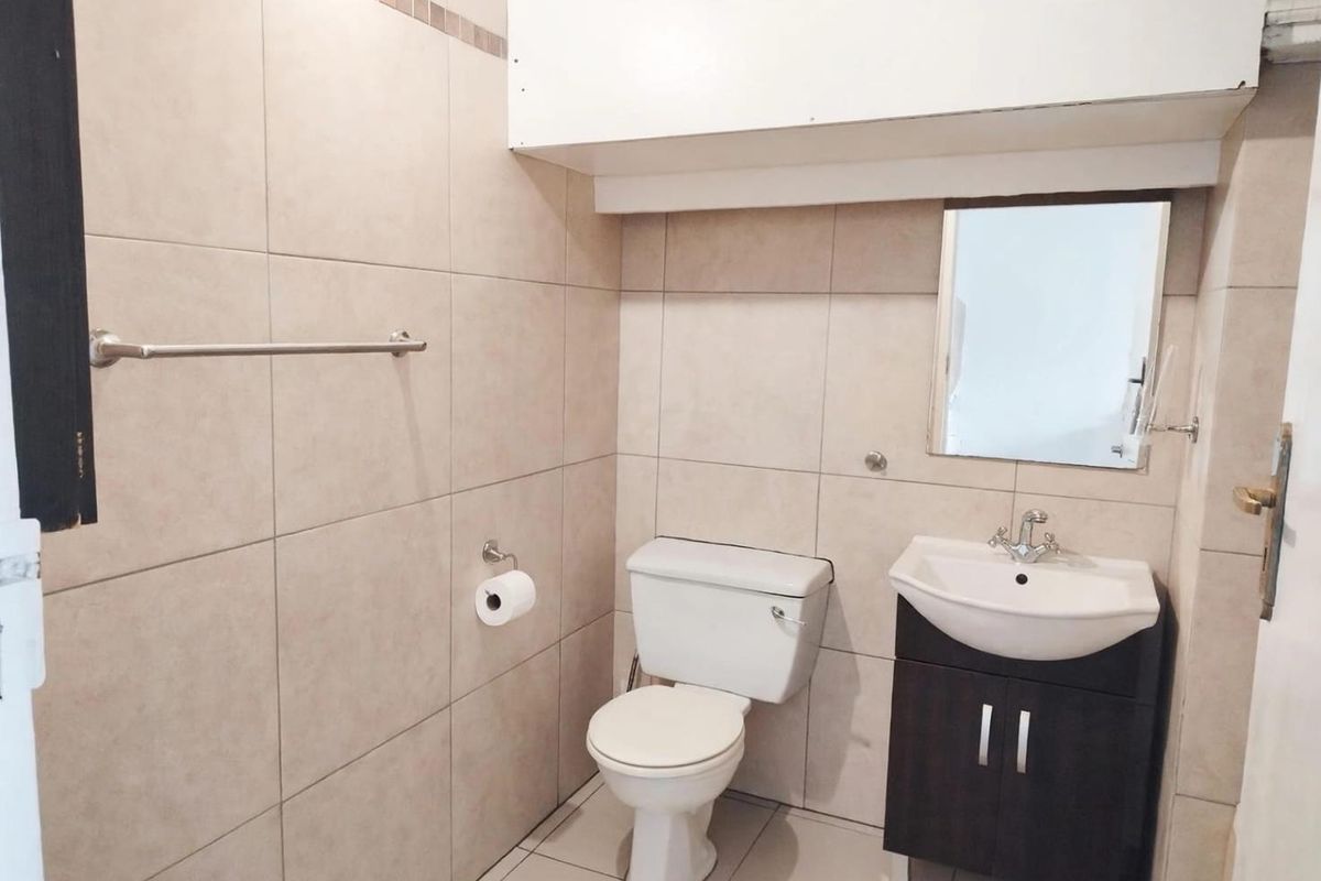 A functional bathroom featuring neutral ceramic wall and floor tiles, a vanity cabinet with a washbasin, and a wall-mounted mirror.