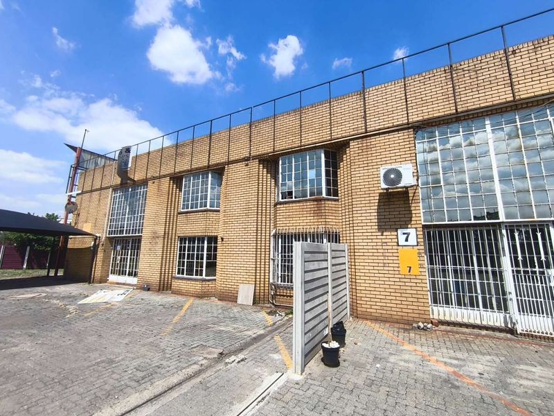 Front elevation of an industrial property featuring a brick facade, paved parking area, security bars, and an external air conditioning unit.
