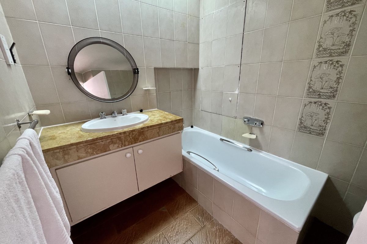 A dated bathroom featuring a built-in vanity with integrated basin, a standard bathtub, and full-height wall tiling in need of modernization.