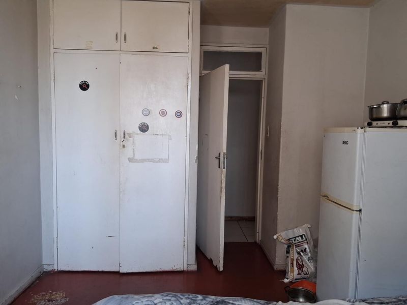 A bedroom featuring built-in cupboards and an internal door, showing significant signs of wear and requiring cosmetic updates to improve the living space.