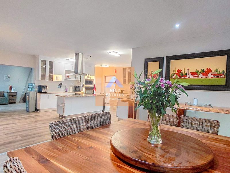 Spacious open-plan living and dining area featuring a modern kitchen with built-in cabinetry, island, and integrated appliances, finished with light laminate flooring.
