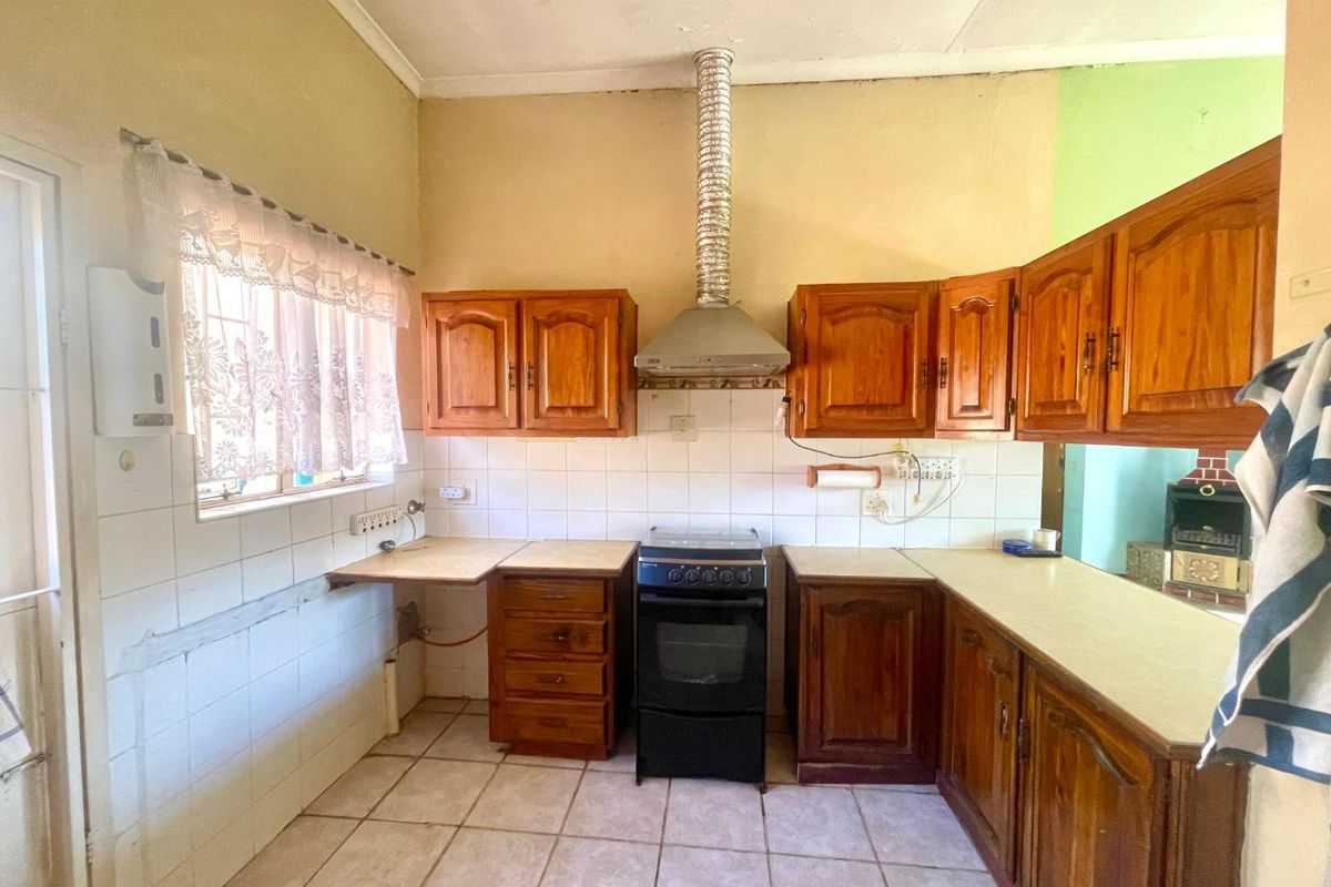 A dated kitchen featuring wooden cabinetry, tiled flooring, a built-in oven with extractor fan, and tiled splashbacks.
