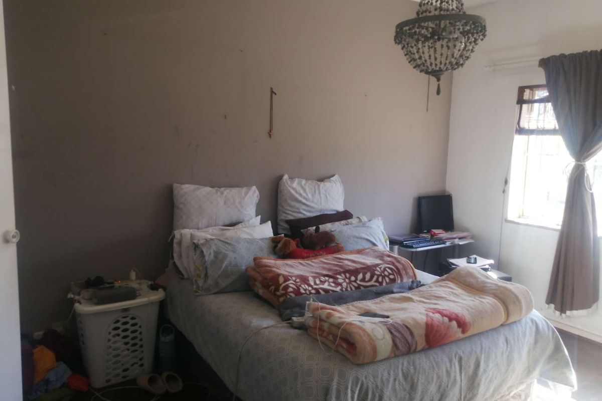A bedroom featuring a decorative chandelier and a window with security bars, providing natural light to the space.