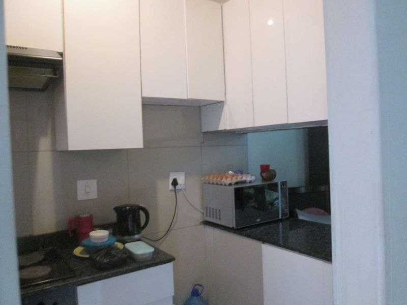 Compact kitchen featuring white cabinetry, dark granite countertops, and a tiled backsplash with an integrated extractor fan.