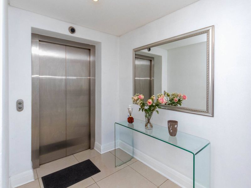 A clean and modern apartment entrance foyer featuring a stainless steel elevator and neutral tiled flooring.