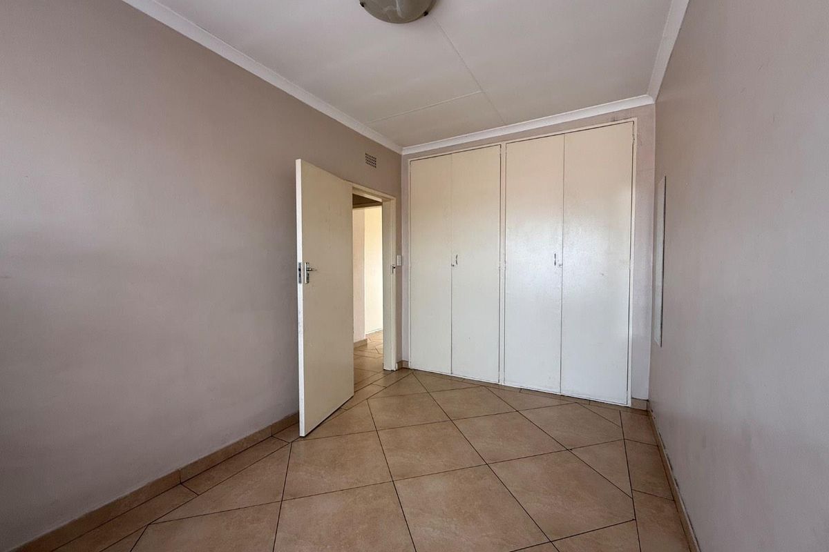 A vacant bedroom featuring built-in cupboards, tiled flooring, and a neutral color palette, offering a clean canvas for personalization.