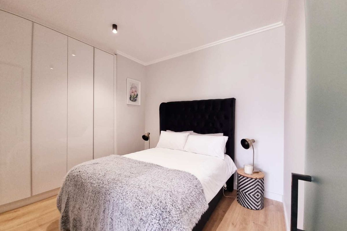 A modern bedroom featuring built-in floor-to-ceiling wardrobes, light wood-look flooring, and recessed ceiling lighting.